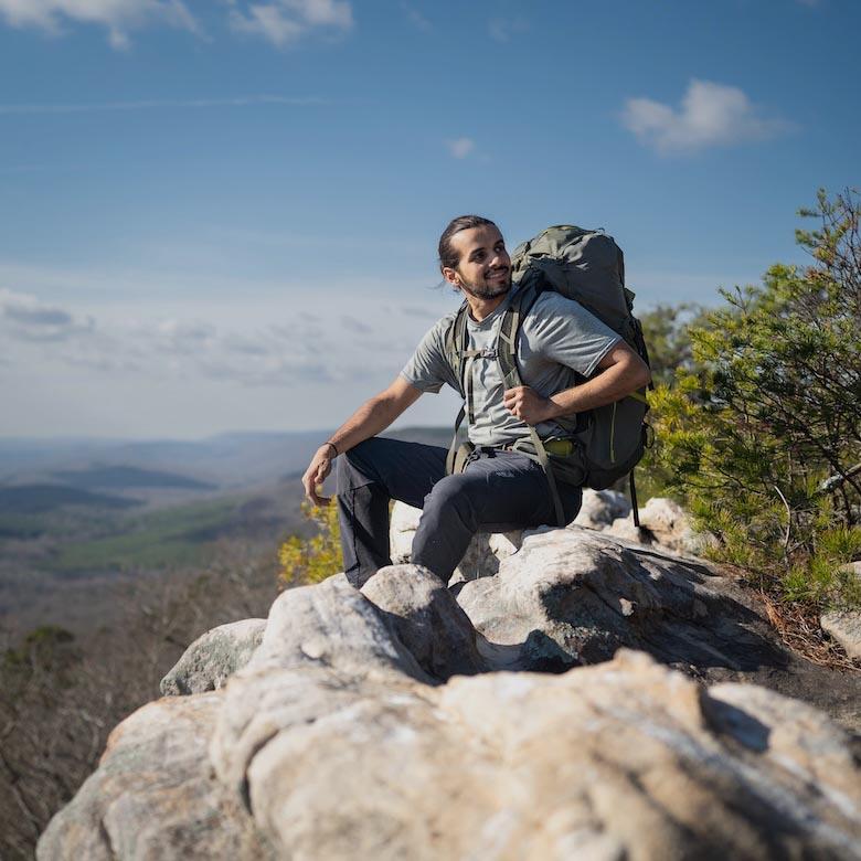 A man with a large backpack sits on a rock with a view from high up
