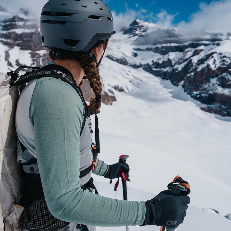 A woman out backcountry skiing looks off toward snow-capped mountains