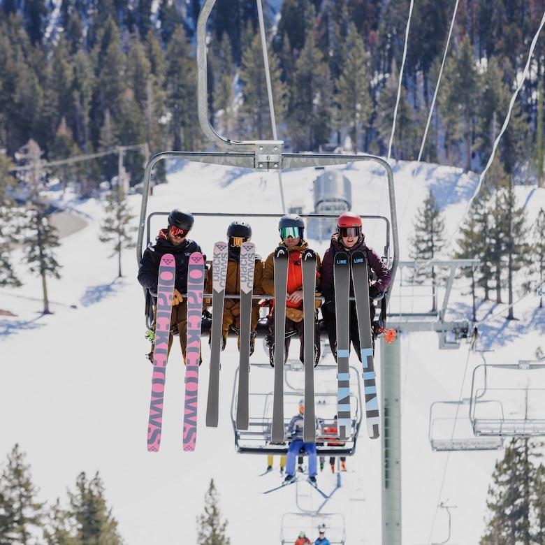 Four people sitting on a ski lift with their legs up to show the underside of their skis