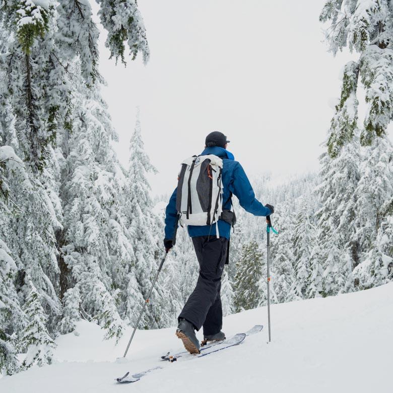 A man skins up a snowy mountain wearing a ski backpack
