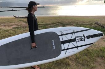 A man carrying a black and white paddle board to the beach at sunset