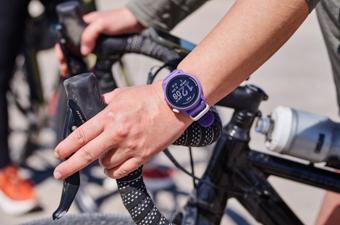 A purple GPS watch on a wrist holding onto bike handlebars