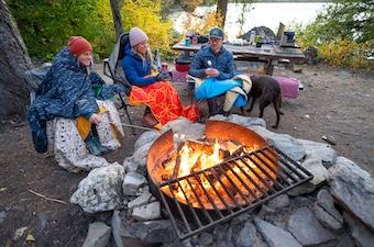 Three members of the Switchback Travel crew sit around a campfire and roast marshmallows