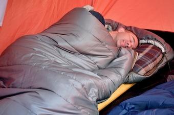 A man drifts off to sleep in a tent in the roomy REI Siesta Hooded 20 sleeping bag