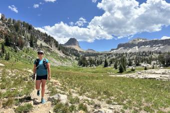 A woman hiking up a backpacking trail with mountain views behind her