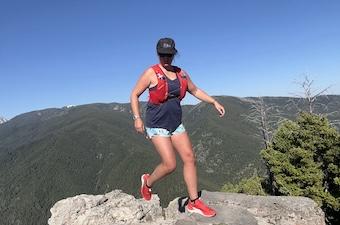 A runner on top of a peak in a red pair of the Salomon Pulsar shoe with a blue sky behind.