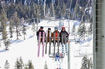 Skiiers show off their skis while riding up a ski lift.