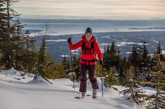 A woman skins up a snowy hill on skis wearing a red synthetic jacket
